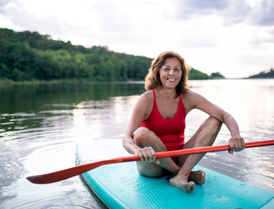 Senior woman paddleboarding on lake in summer. Copy space