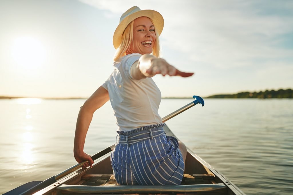 Smiling woman reaching out her hand while paddling a canoe